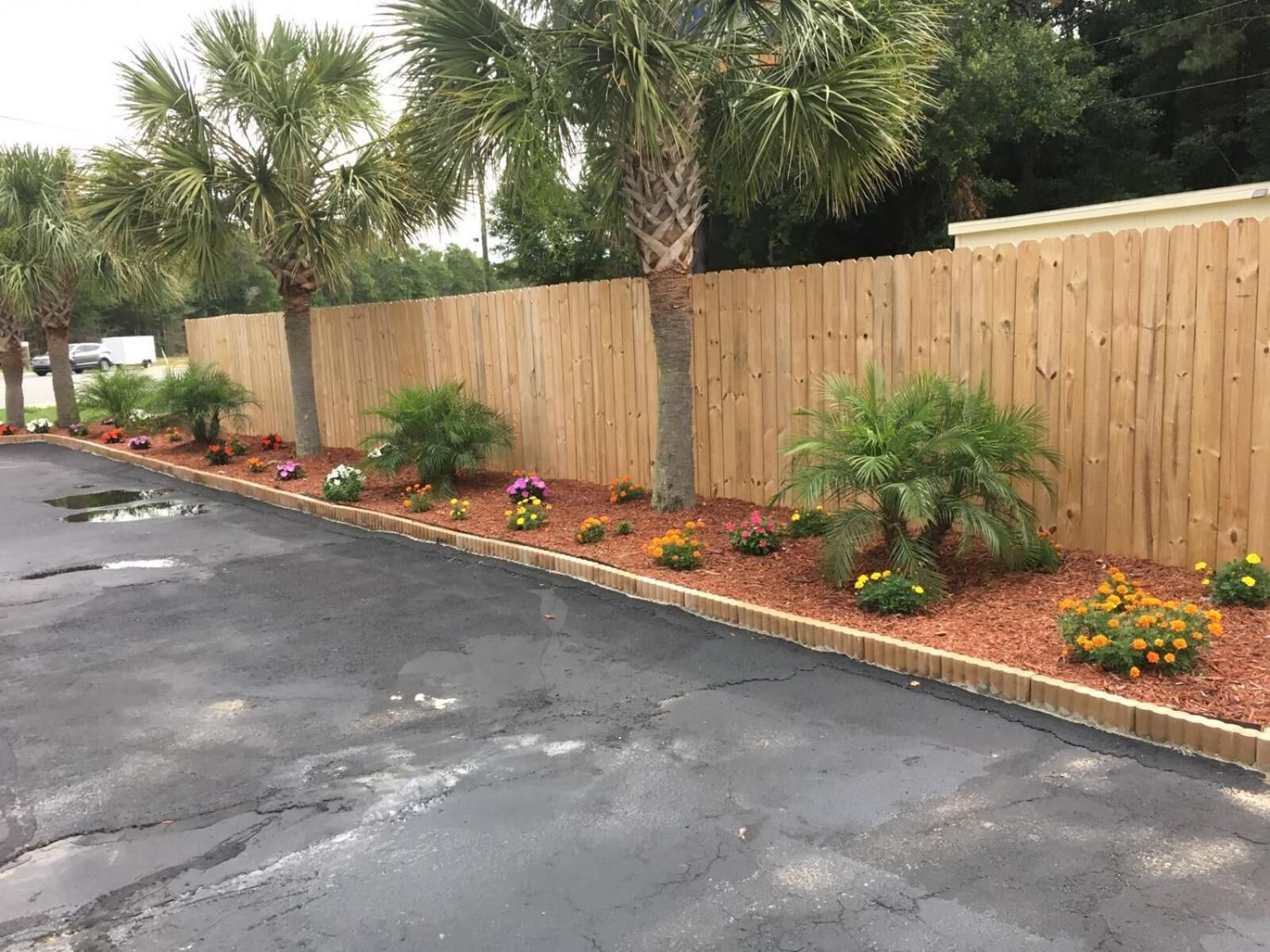 Een parkeerplaats met een houten hek en een bloembed met verschillende planten en bloemen.