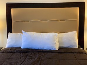 Un lit avec une couette marron foncé, deux oreillers blancs et une tête de lit recouverte d’un tissu beige.
