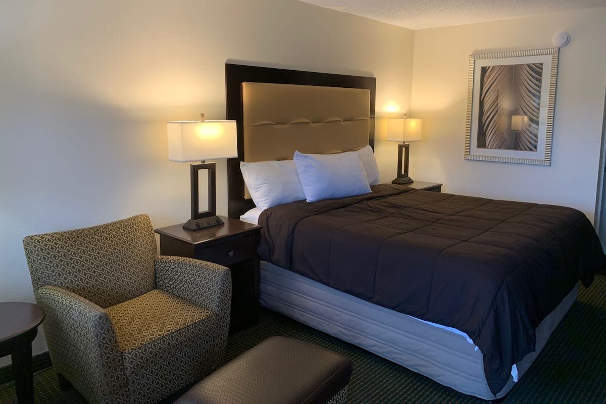 A hotel room with a large bed, two bedside tables with lamps, a patterned armchair, and a bench.