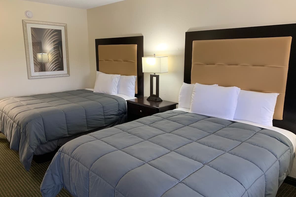 A hotel room with two beds, each with a headboard and pillows, and a bedside table with a lamp.