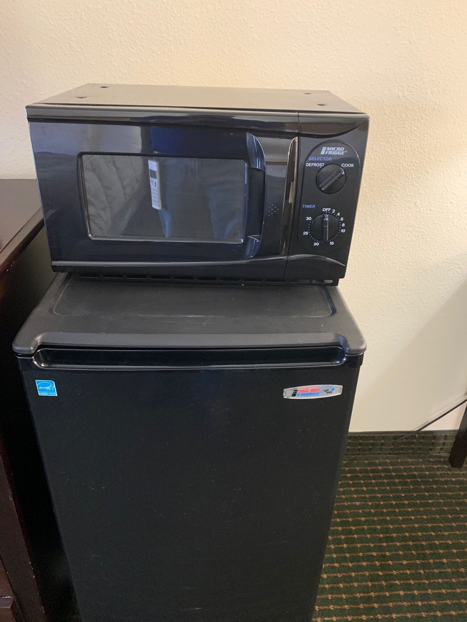 A black refrigerator with a microwave on top.