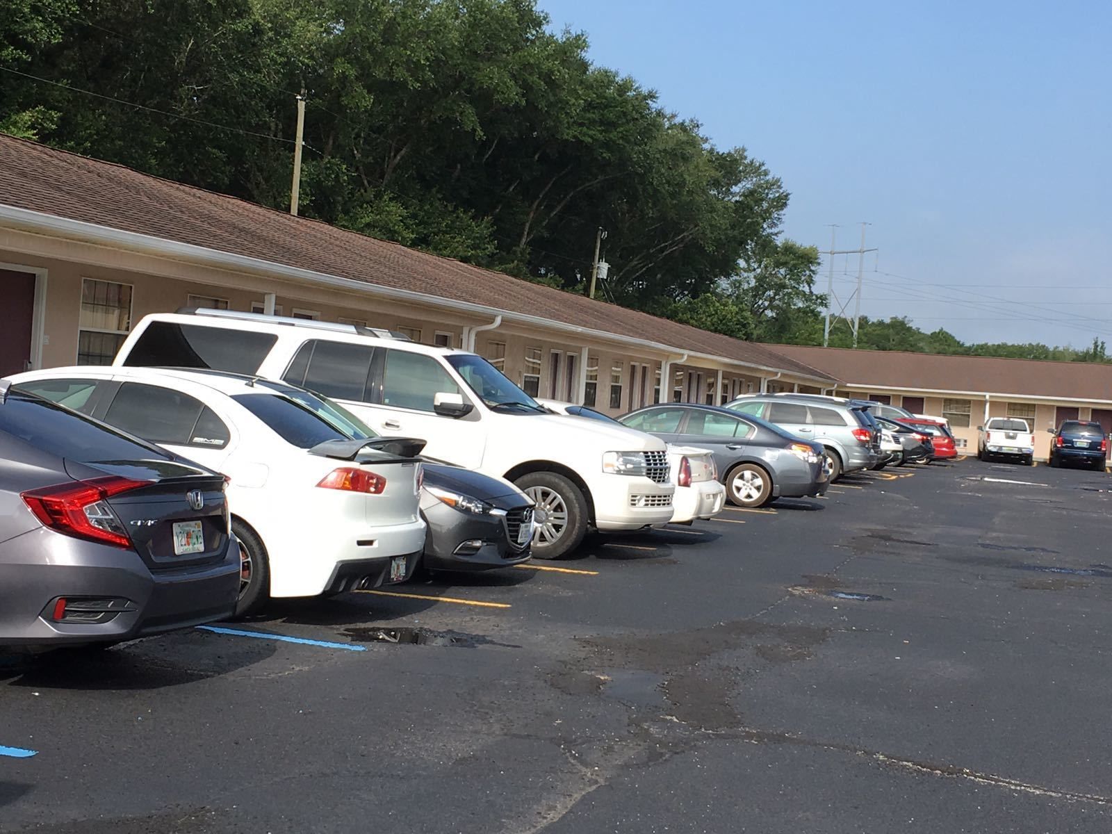 Fila de coches aparcados en un aparcamiento, con un motel al fondo.