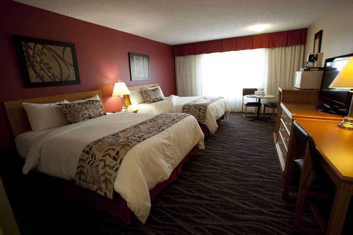 Quarto de hotel com duas camas, uma escrivaninha, uma cadeira, um abajur, uma cafeteira e uma televisão.