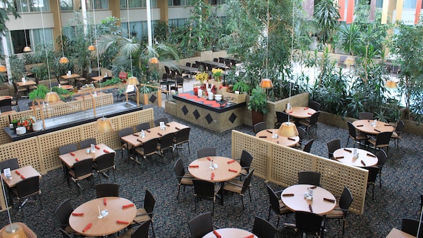A spacious indoor dining area with multiple tables and chairs, surrounded by lush greenery and potted plants. - Westlock Inn and Conference Centre (Westlock)