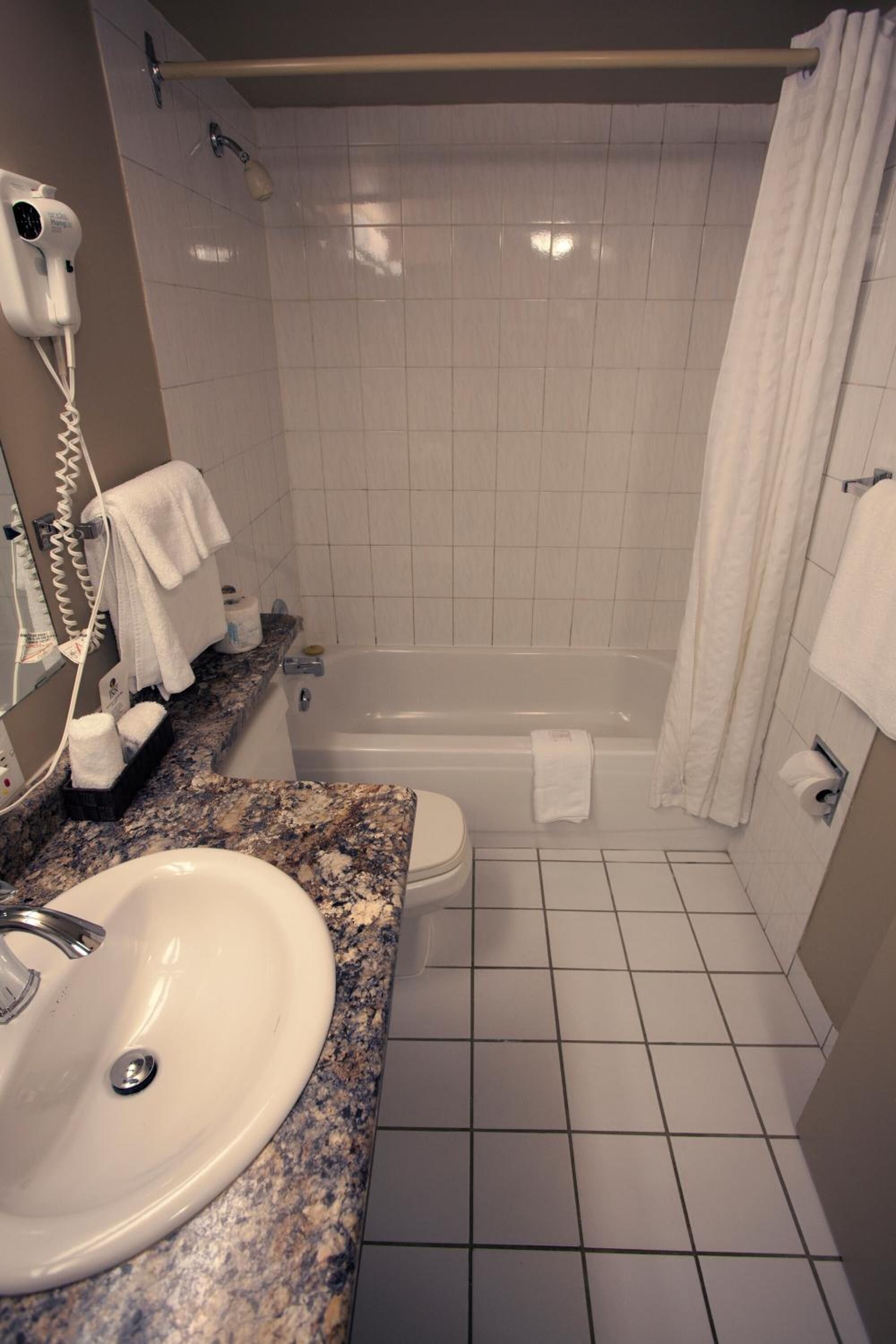 A bathroom with a sink, toilet, and bathtub. There is a hairdryer on the wall, and towels are hanging on the wall and on the bathtub.