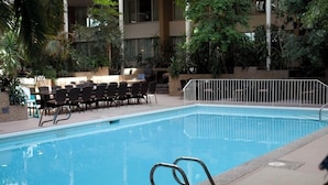 An indoor swimming pool with a clear blue water, surrounded by a metal railing, and a seating area with chairs and tables. - Westlock Inn and Conference Centre (Westlock)
