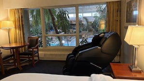 A hotel room with a massage chair, a bed, a desk, and a large window with a view of palm trees and a pool. - Westlock Inn and Conference Centre (Westlock)