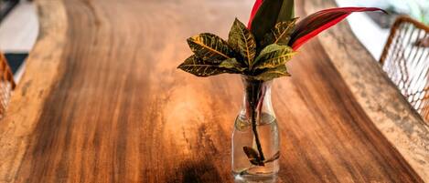 A wooden dining table with a clear glass vase containing a plant with red leaves.