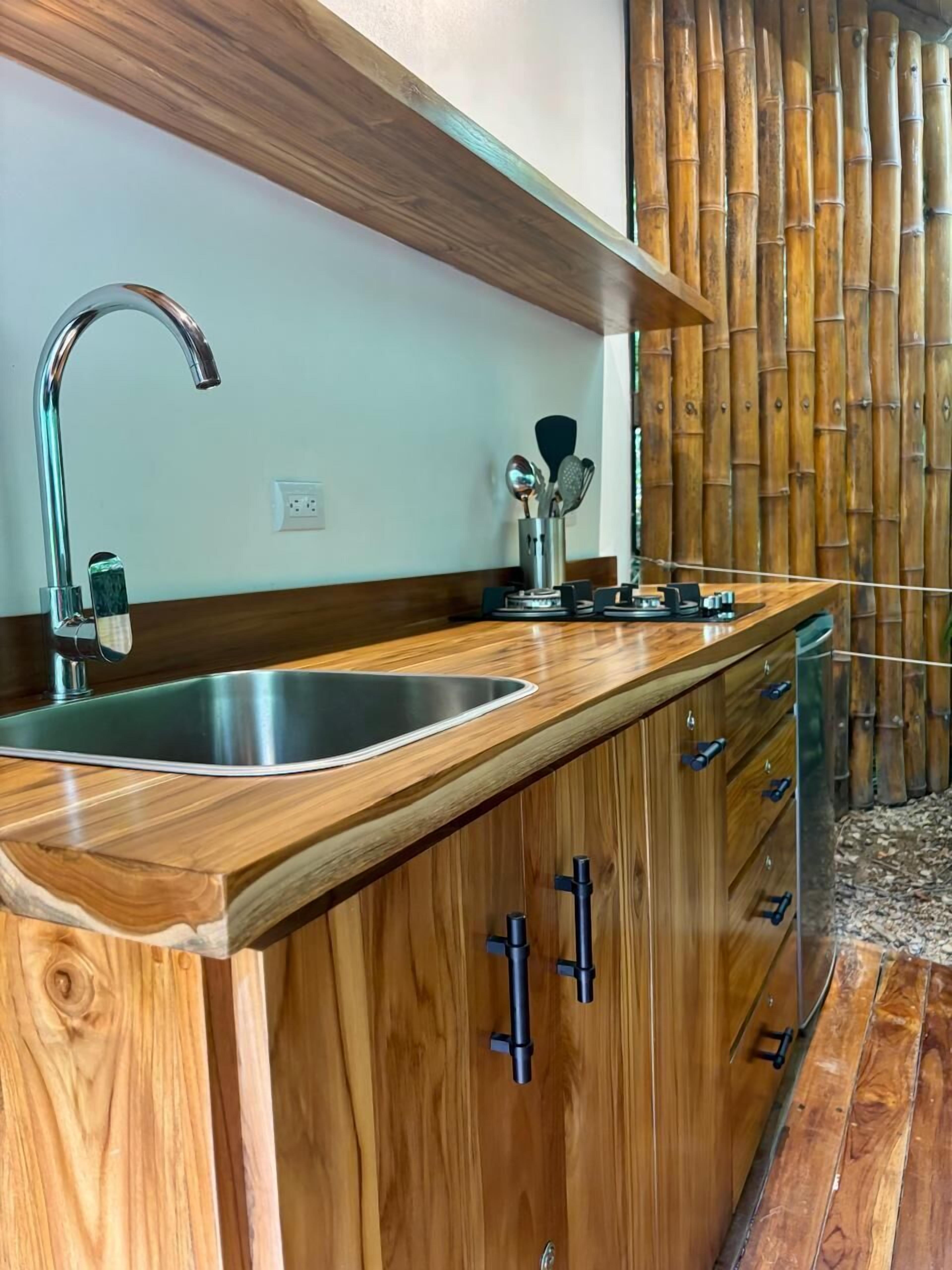 A kitchen with a wooden countertop, stainless steel sink, and black cabinets.