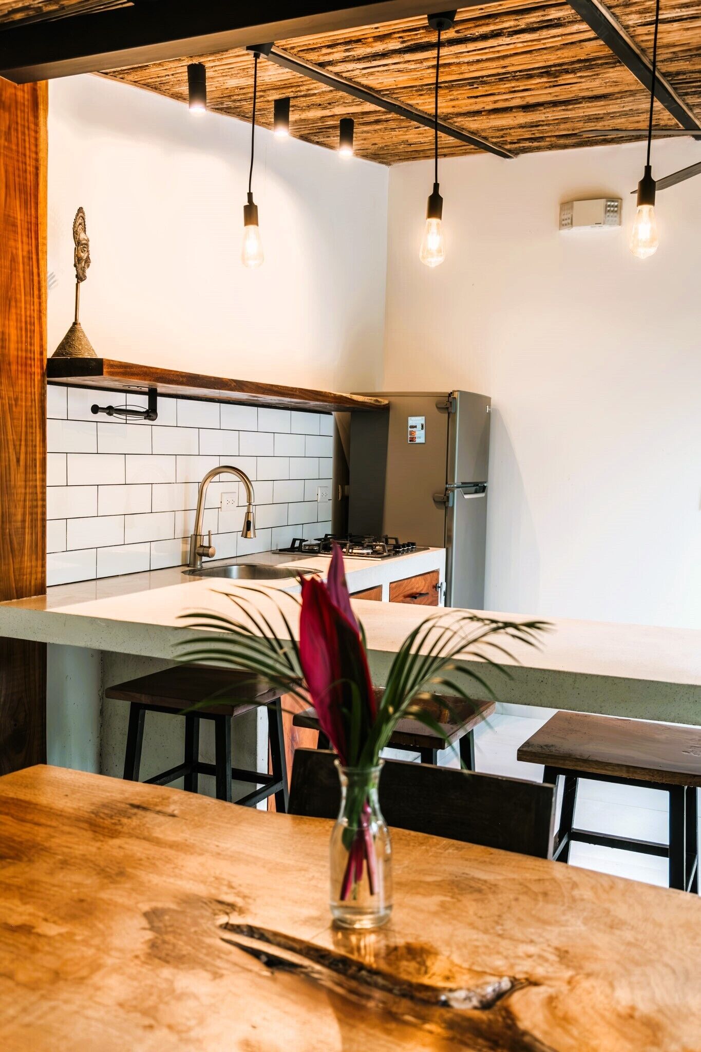 A modern kitchen with a white tiled backsplash, stainless steel appliances, and hanging pendant lights.