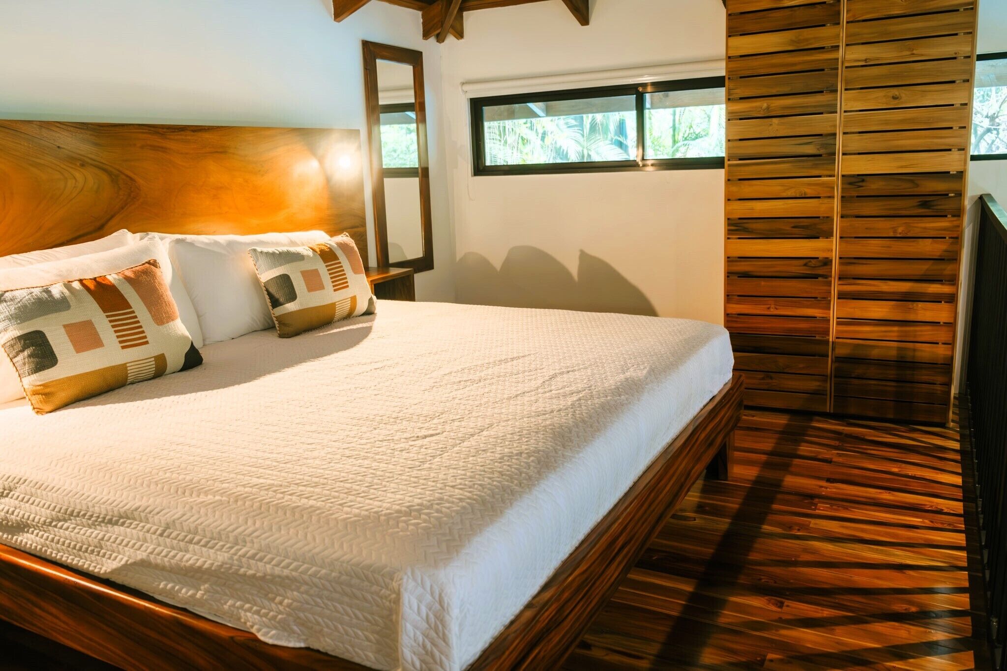 A neatly made bed with a white quilt, a wooden headboard, and two pillows with geometric patterns.