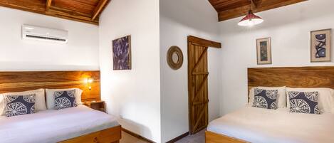 A room with two wooden beds, white walls, wooden ceiling beams, and a ceiling fan.