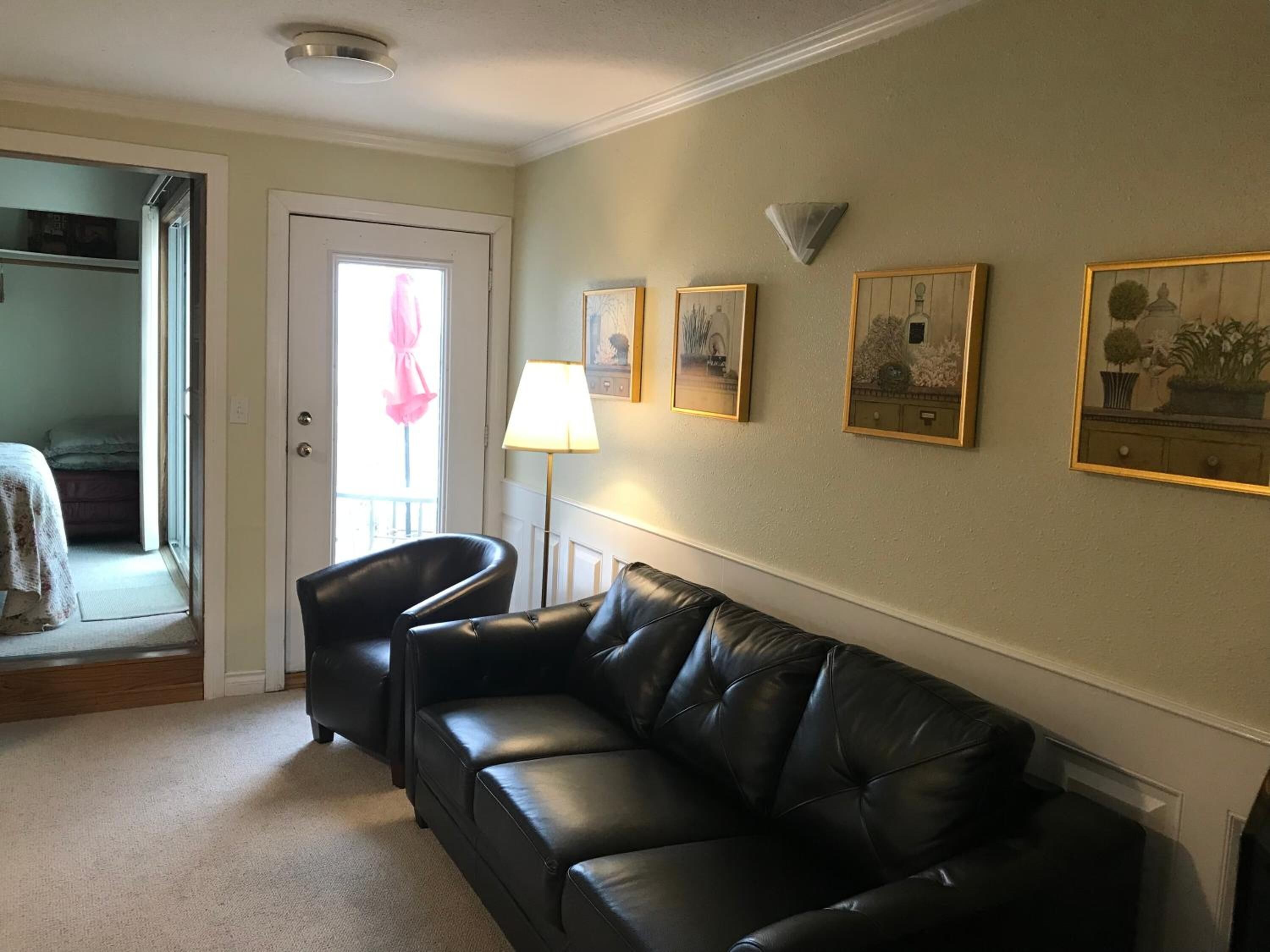 A living room with a black leather sofa, a lamp, and framed pictures on the wall.