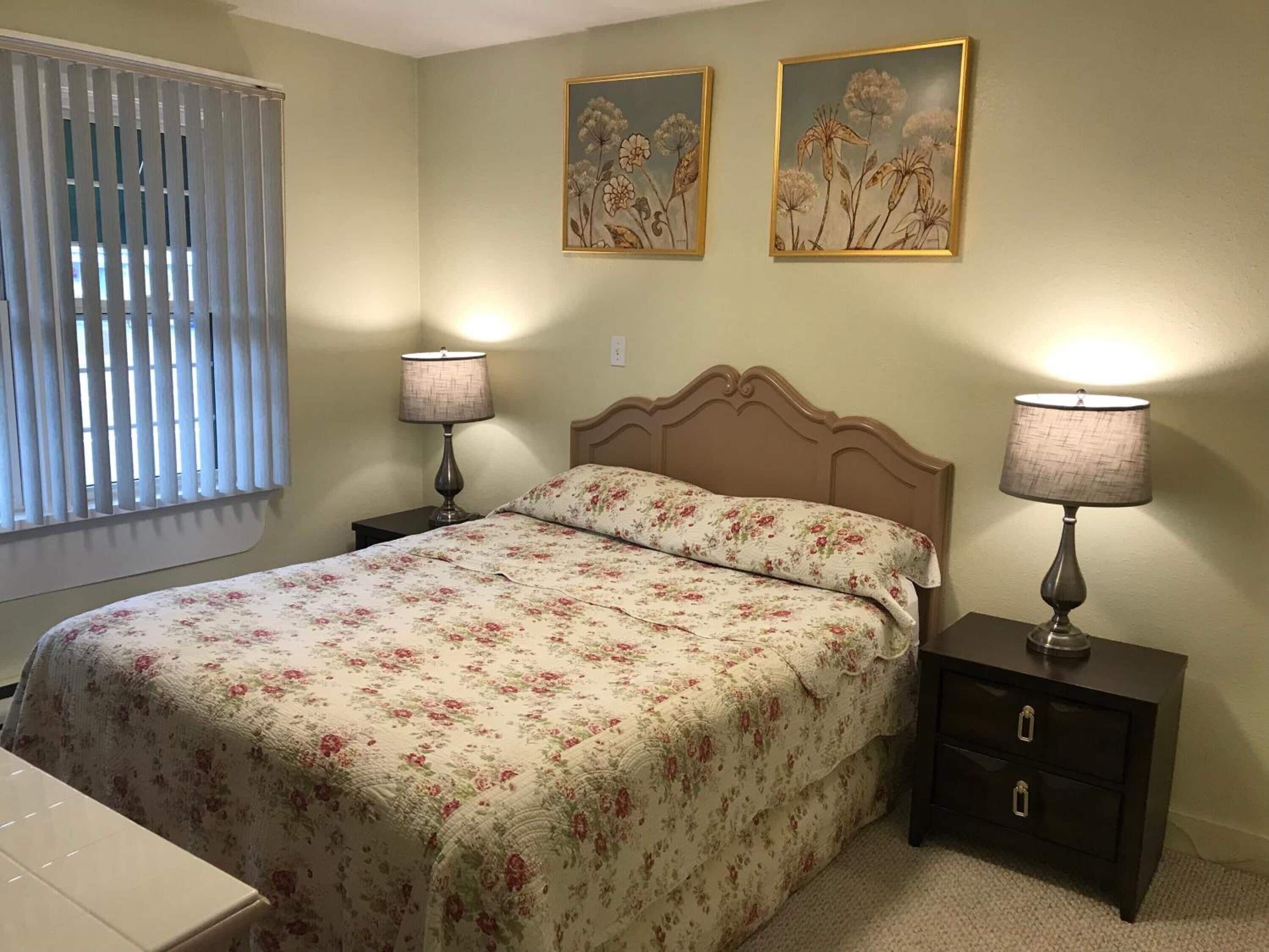 A bedroom with a bed, two bedside tables, a nightstand, and two wall-mounted paintings.