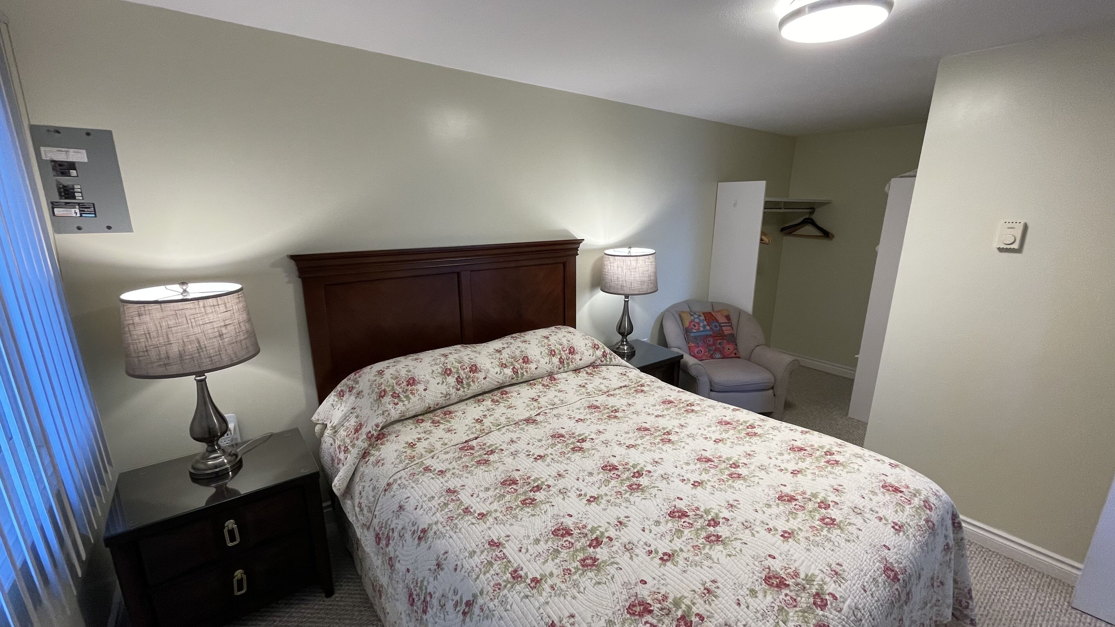 Une chambre à coucher comprenant un lit, deux lampes de chevet, une table de chevet, une chaise et une armoire.