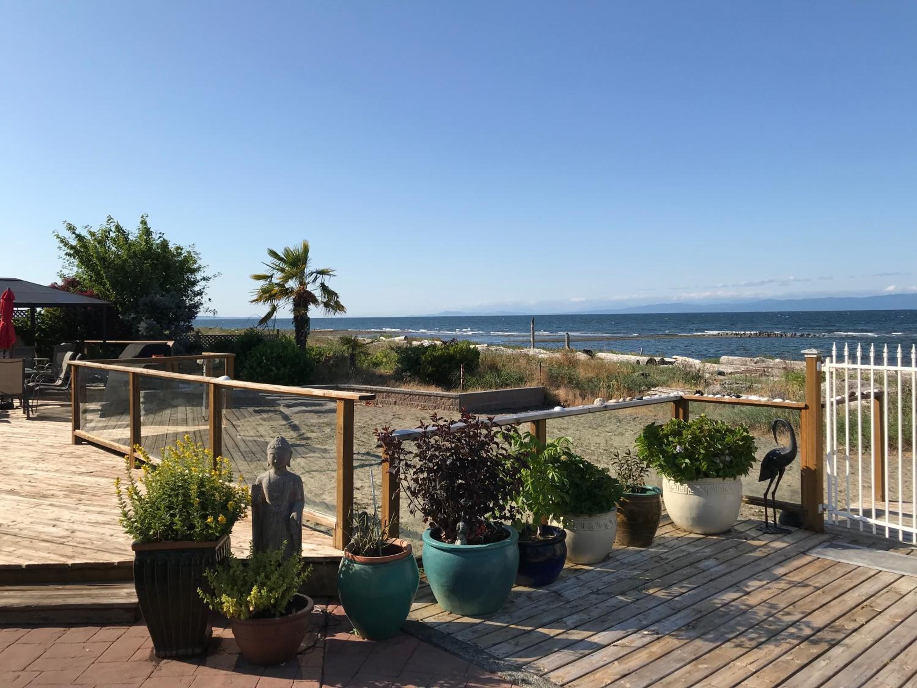A wooden deck with potted plants, a statue, and a view of the ocean.