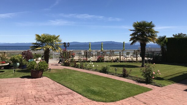 Uma área de pátio com vista para o mar e montanhas, com plantas em vasos, mobiliário de exterior e um gramado bem cuidado.