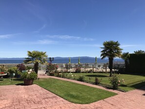 Un patio con vistas al mar y a las montañas, con plantas en macetas, mobiliario exterior y un césped bien cuidado.