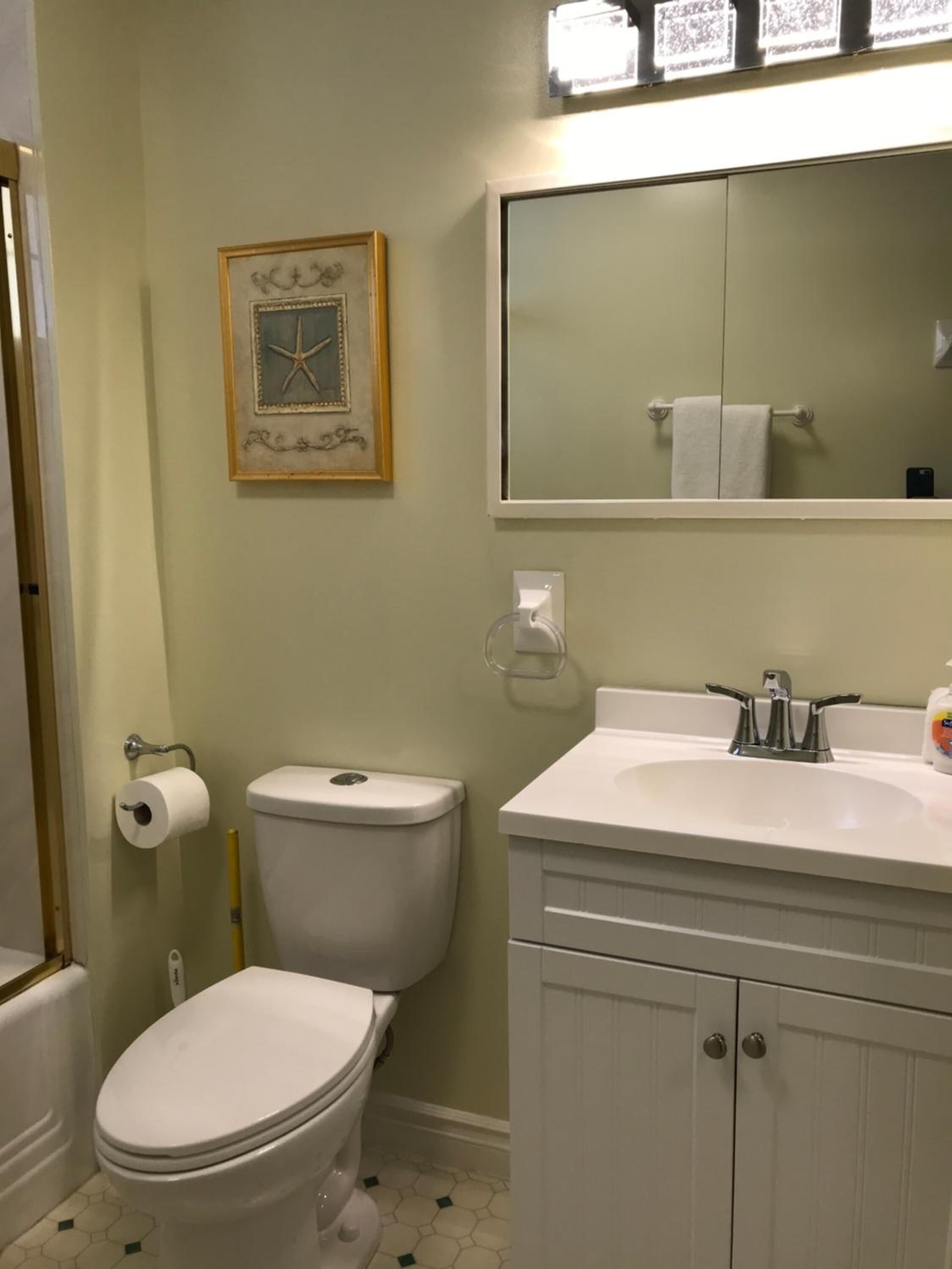 Un baño con inodoro, lavamanos, espejo y un cuadro en la pared.