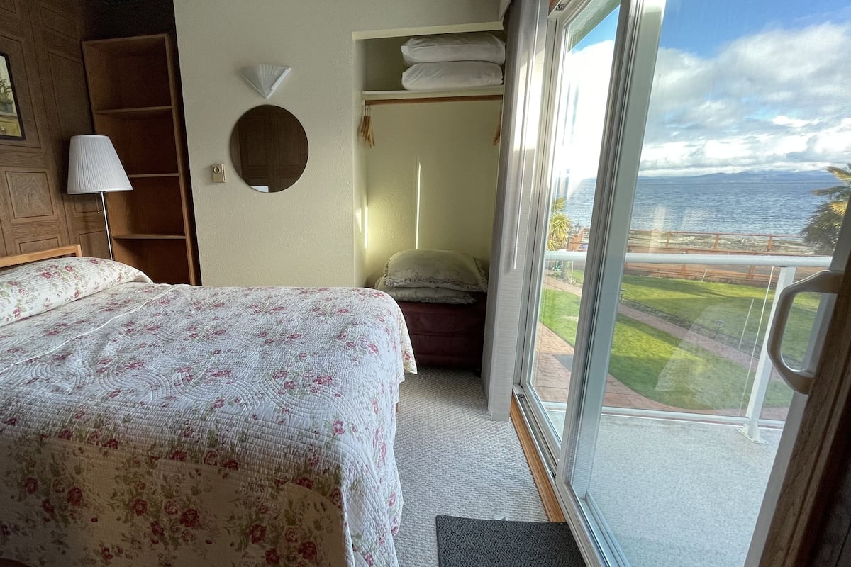 Un dormitorio con cama, mesita de noche, lámpara, armario y vista al mar.