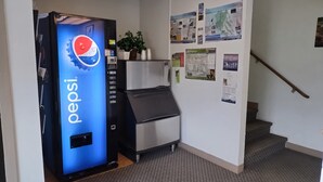A vending machine with a Pepsi logo, a small plant on top, and a wall with various informational posters. - Northgate Inn Motel (Challis)