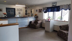 A reception area with a 'Welcome' sign, a key drop box, and a chair near the window. - Northgate Inn Motel (Challis)