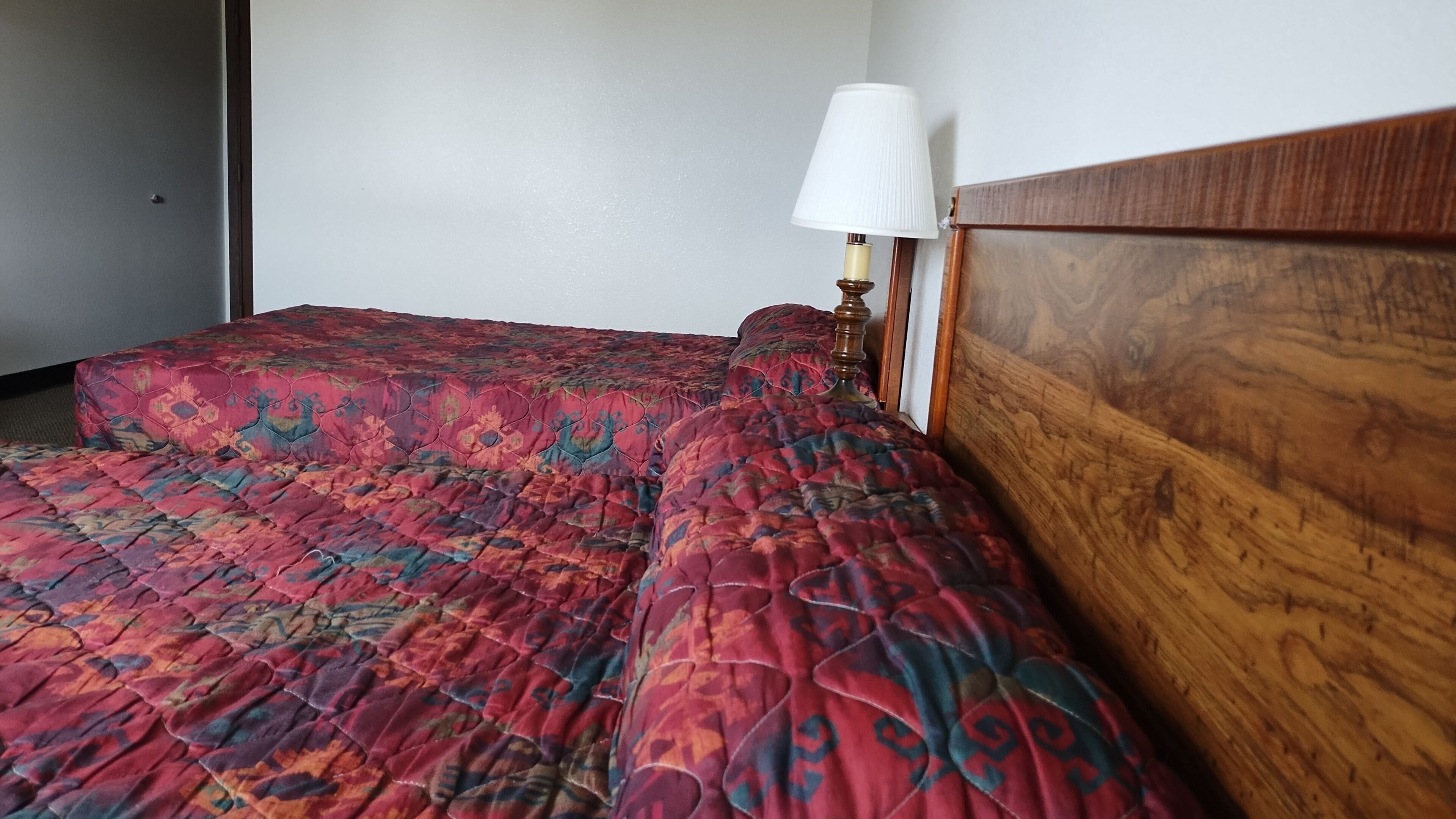 Una habitación con dos camas, cada una con una colcha estampada, un cabecero de madera y una lámpara de noche.