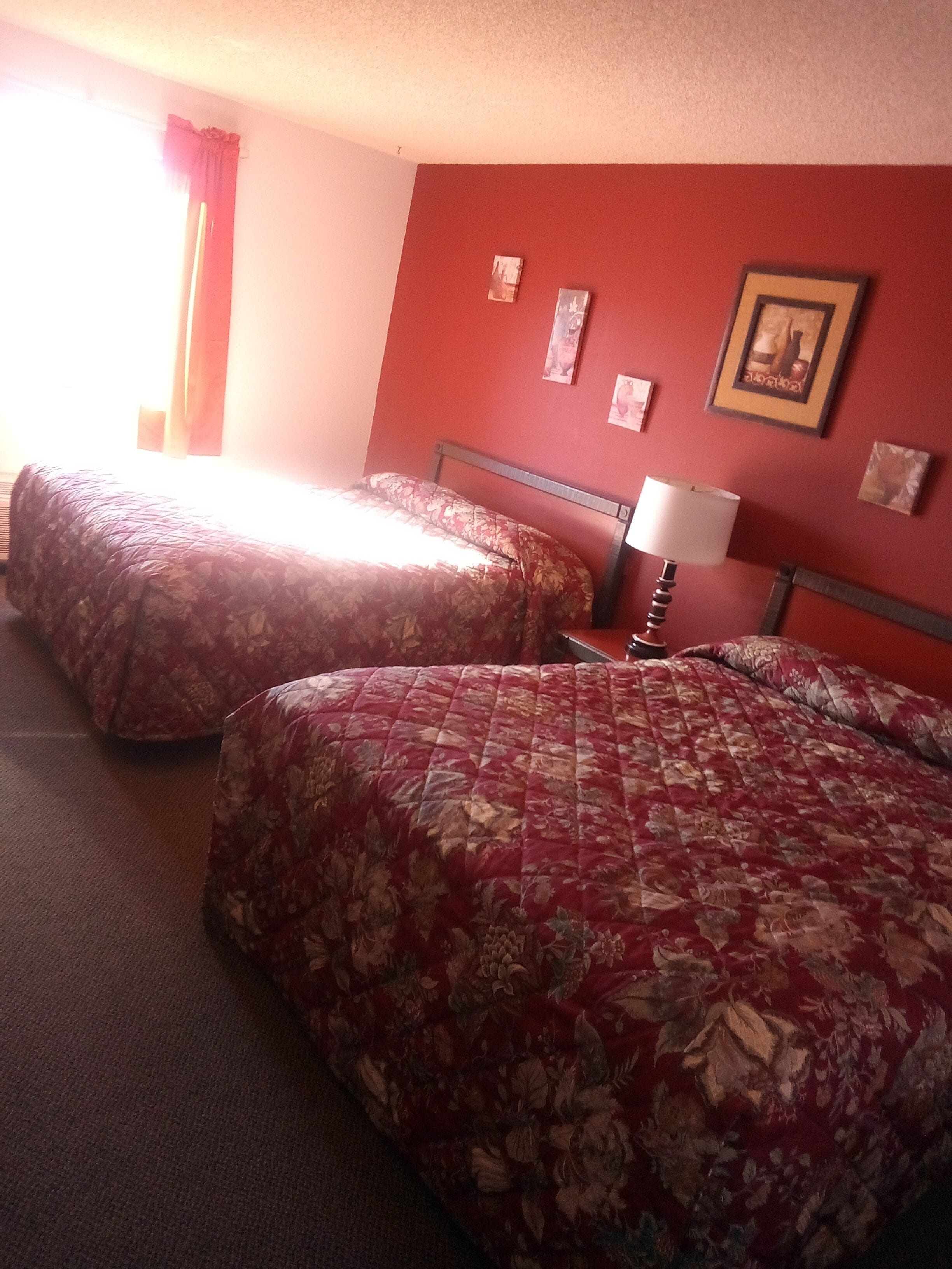 Habitación de hotel con dos camas, una pared roja y un cuadro enmarcado.