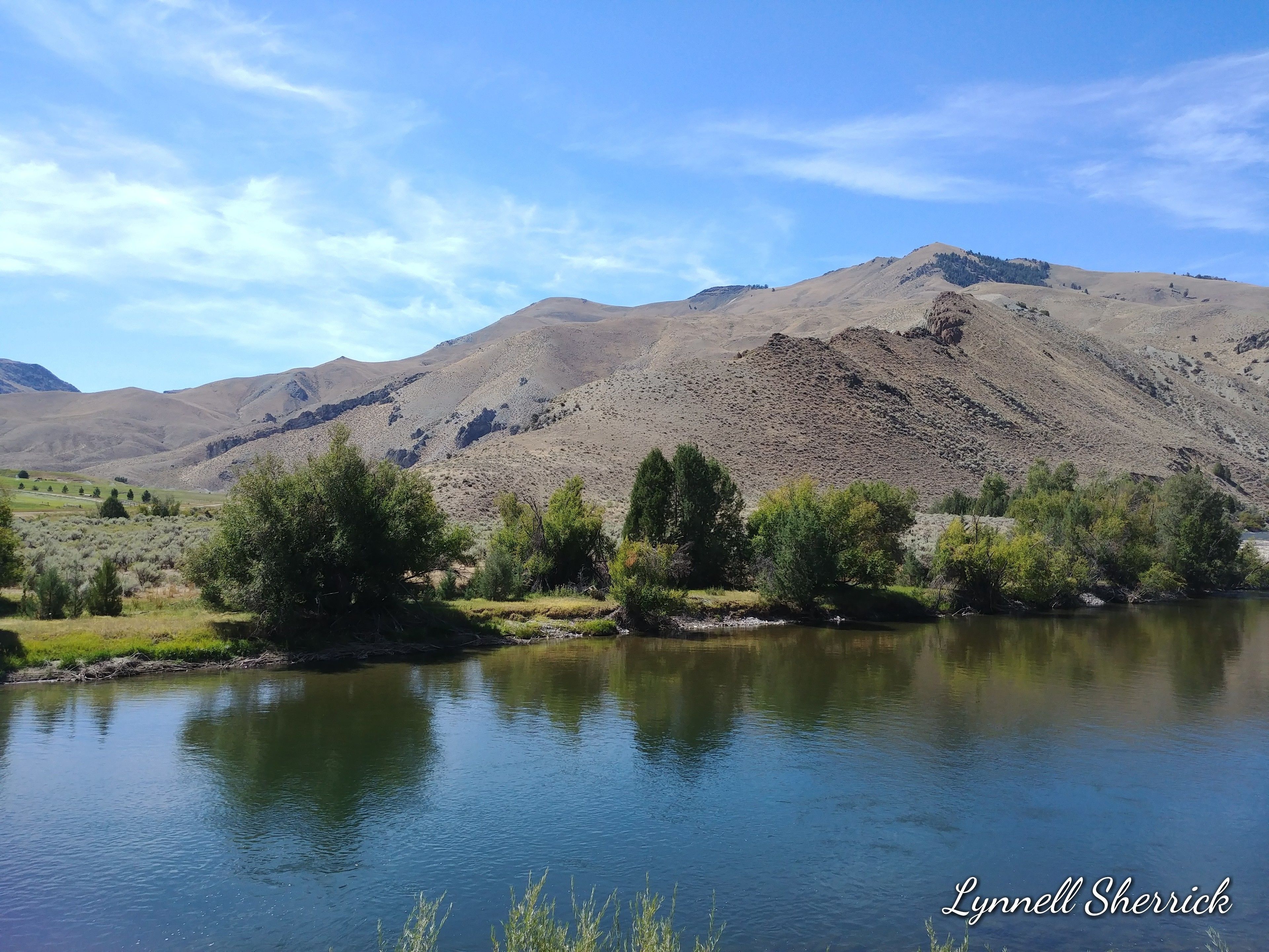 A calm river with mountains in the background and sparse vegetation along the banks.