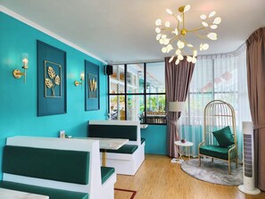A modern living room with teal walls, a large window, a ceiling light fixture, and a green chair. - Phaithong Sotel Resort (Chalong)