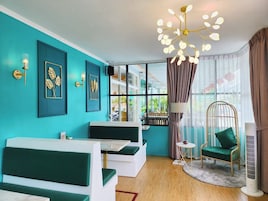 Un soggiorno moderno con pareti color acquamarina, una grande finestra, un lampadario e una poltrona verde.