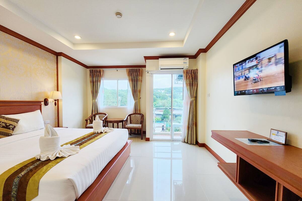 Habitación de hotel con una cama grande, televisión, escritorio y balcón con cortinas.