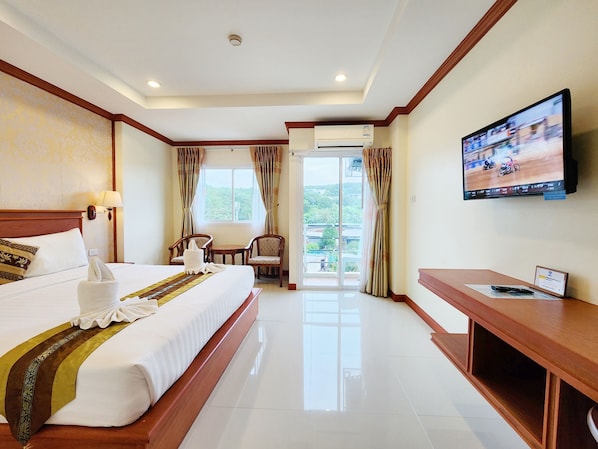 Quarto de hotel com cama grande, televisão, escrivaninha e varanda com cortinas.