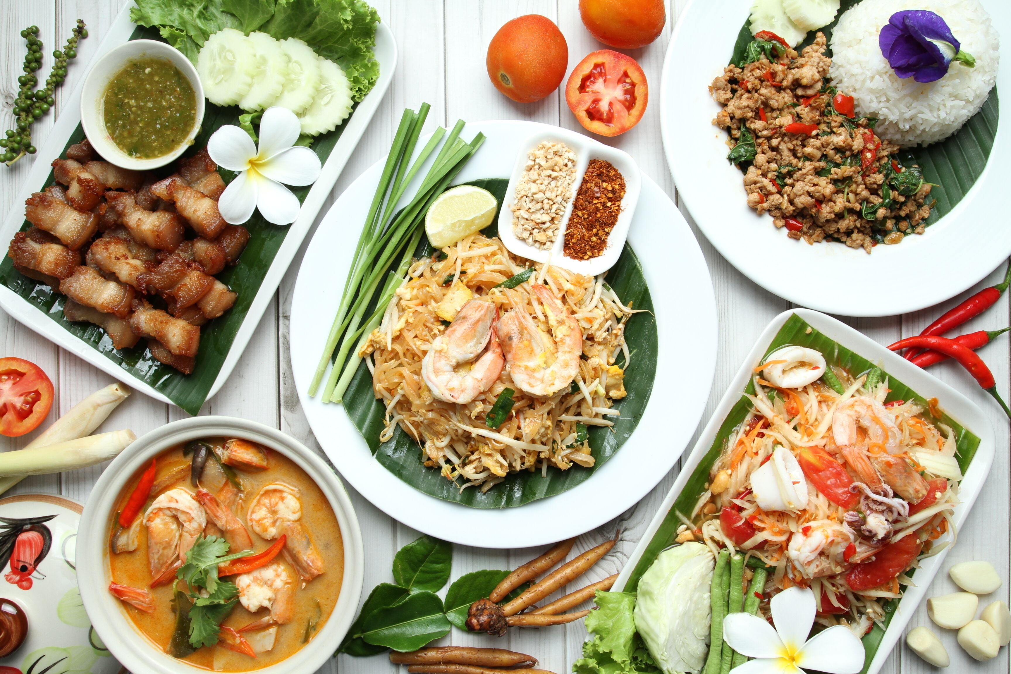 Une variété de plats thaïlandais, notamment le Pad Thaï, la soupe Tom Yum et une assiette de porc croustillant.