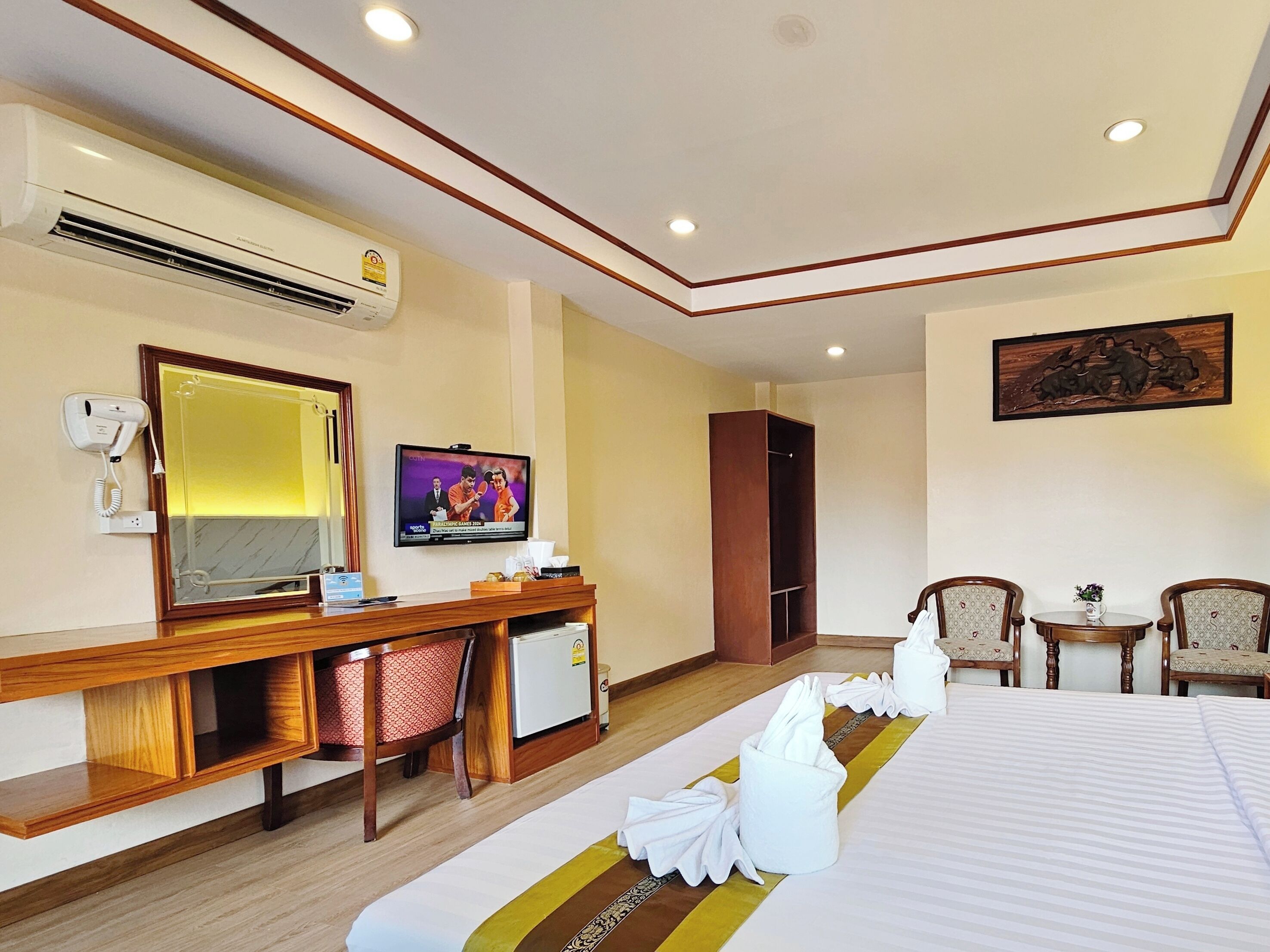 Une chambre d’hôtel comprenant un lit, un bureau avec un ordinateur, une télévision, une armoire et un coin salon avec des fauteuils.