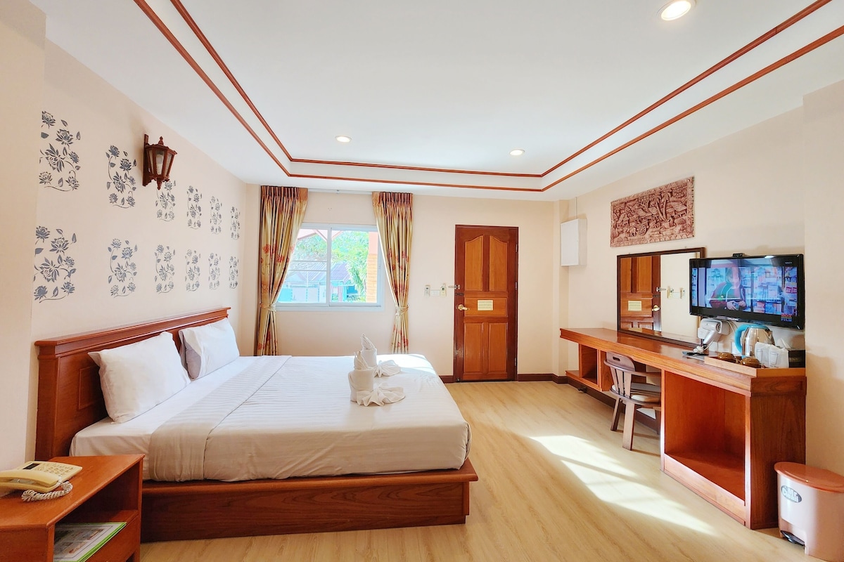 Quarto de hotel com uma cama grande, uma escrivaninha com computador, uma televisão e uma janela com cortinas.