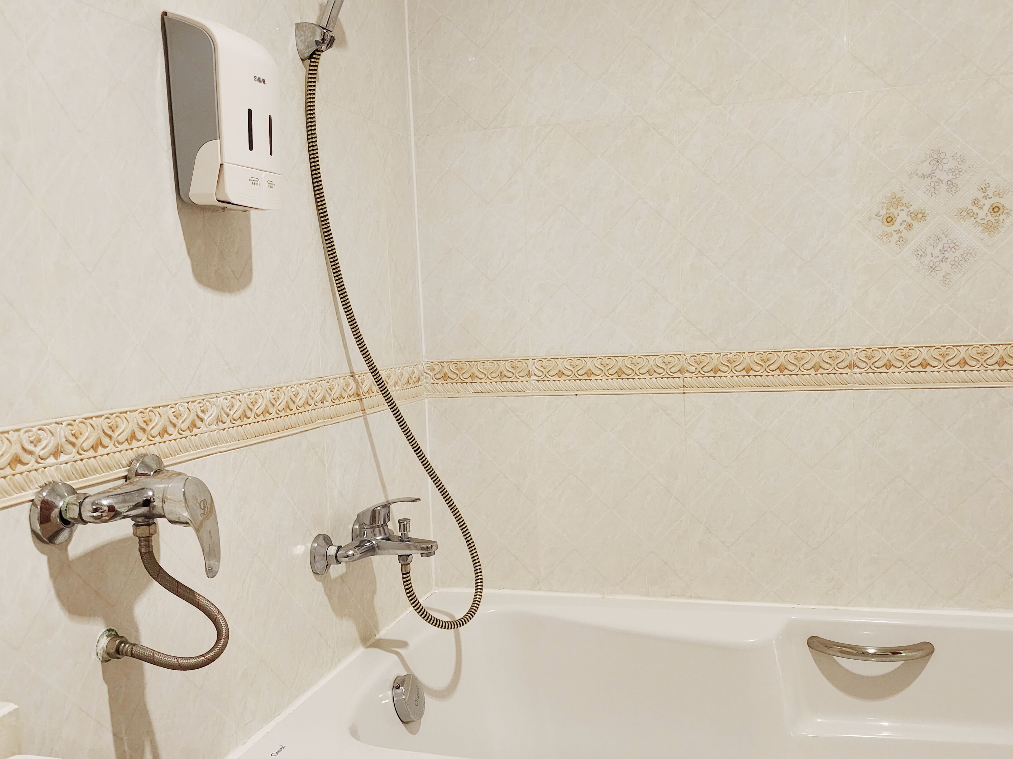 A bathroom with a white bathtub, a handheld showerhead, and a wall-mounted hairdryer.