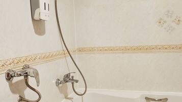 A bathroom with a white bathtub, a handheld showerhead, and a wall-mounted hairdryer.