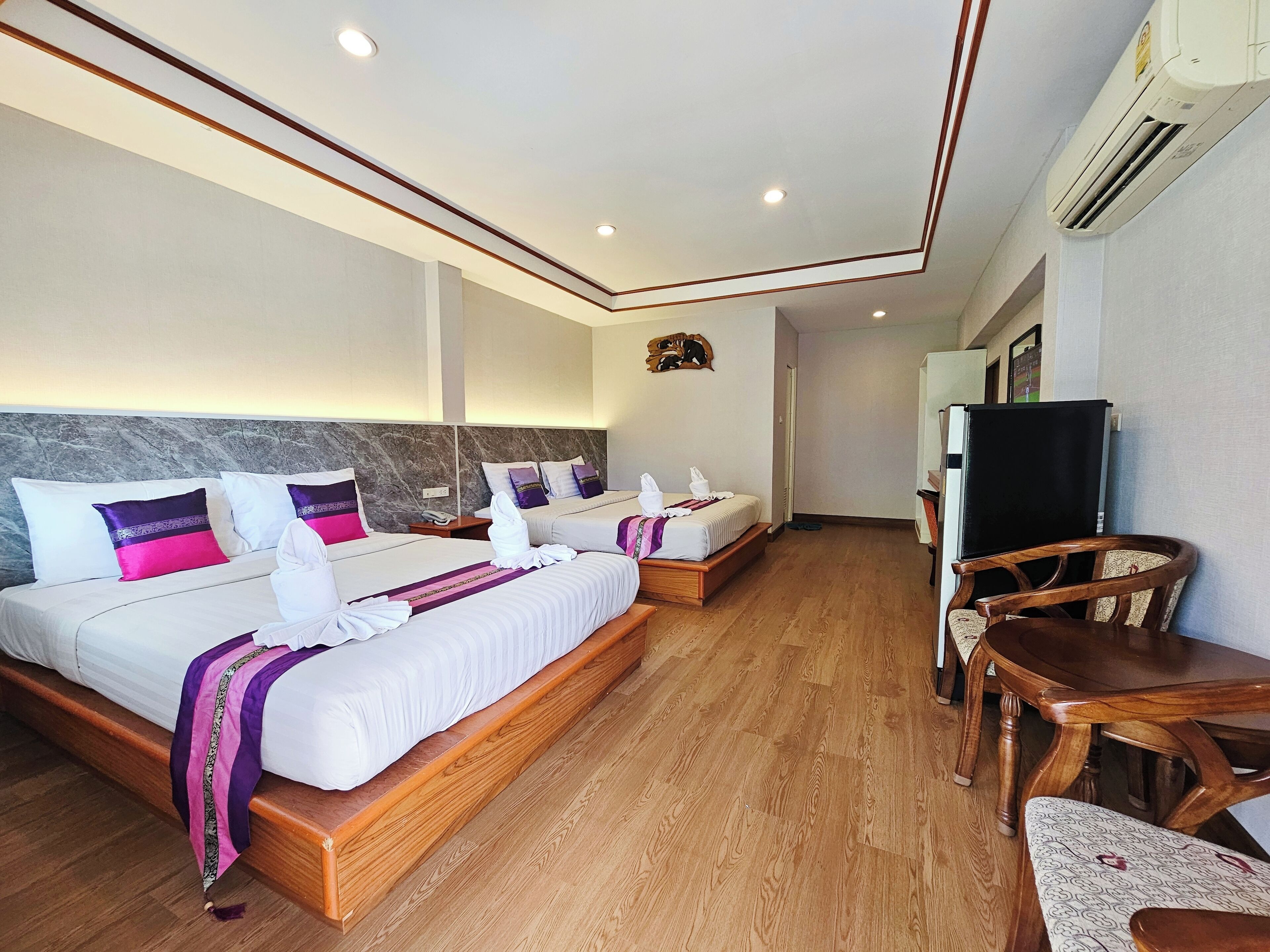 A hotel room with two beds, a wooden floor, a TV, and a dining area.