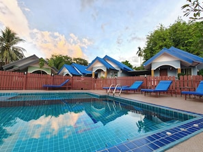 A swimming pool with blue tiles, surrounded by lounge chairs and a wooden fence.