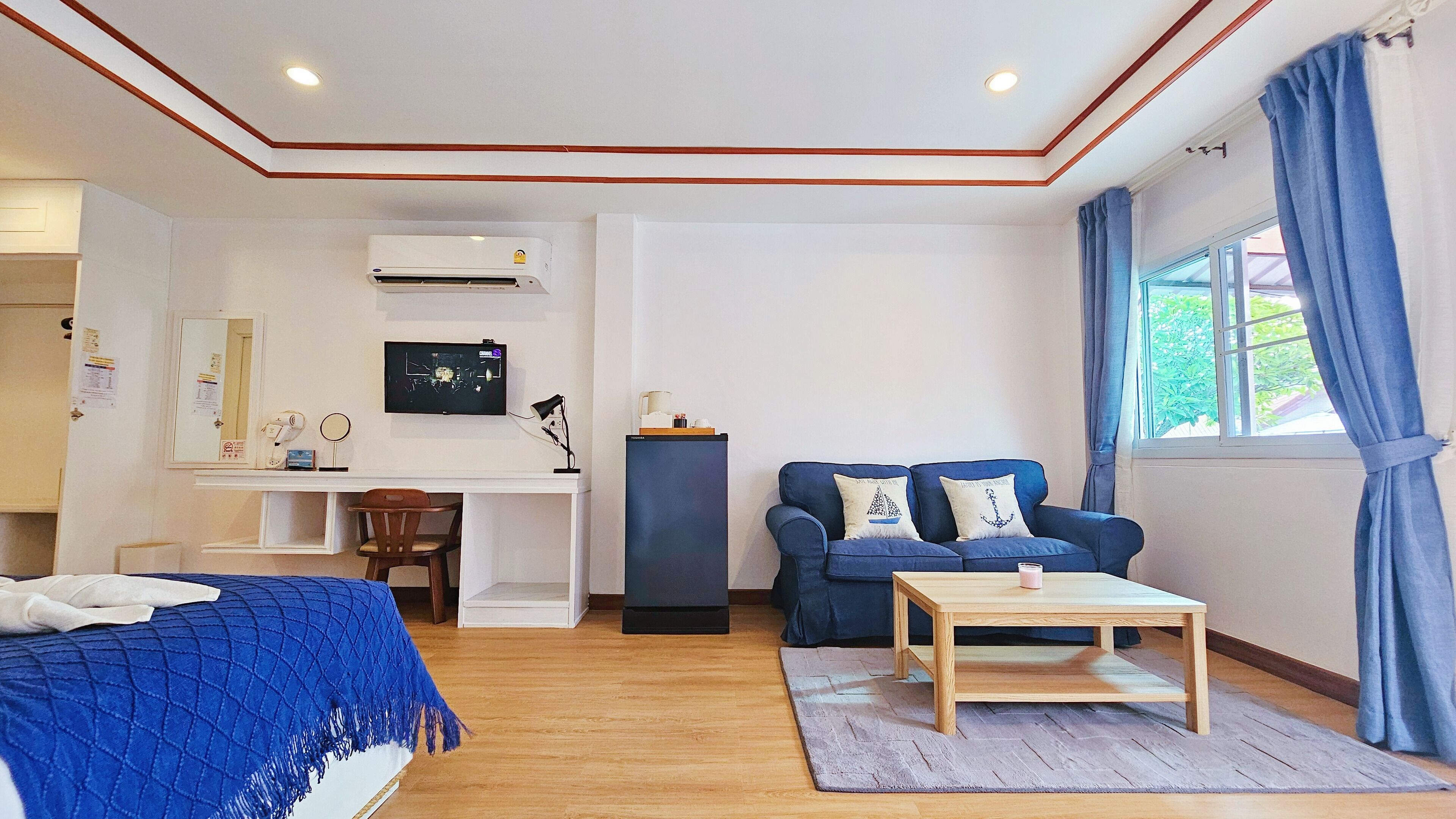 Una habitación de hotel moderna con una cama, un escritorio con computadora, un sofá azul y una ventana con cortinas.
