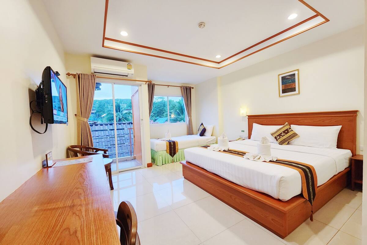 Habitación de hotel con una cama de madera, un televisor montado en la pared, una mesa de comedor y vistas al exterior a través de la puerta corrediza.