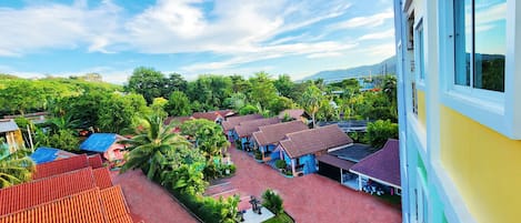 A view of a hotel courtyard with multiple buildings, a red-tiled roof, and lush greenery.