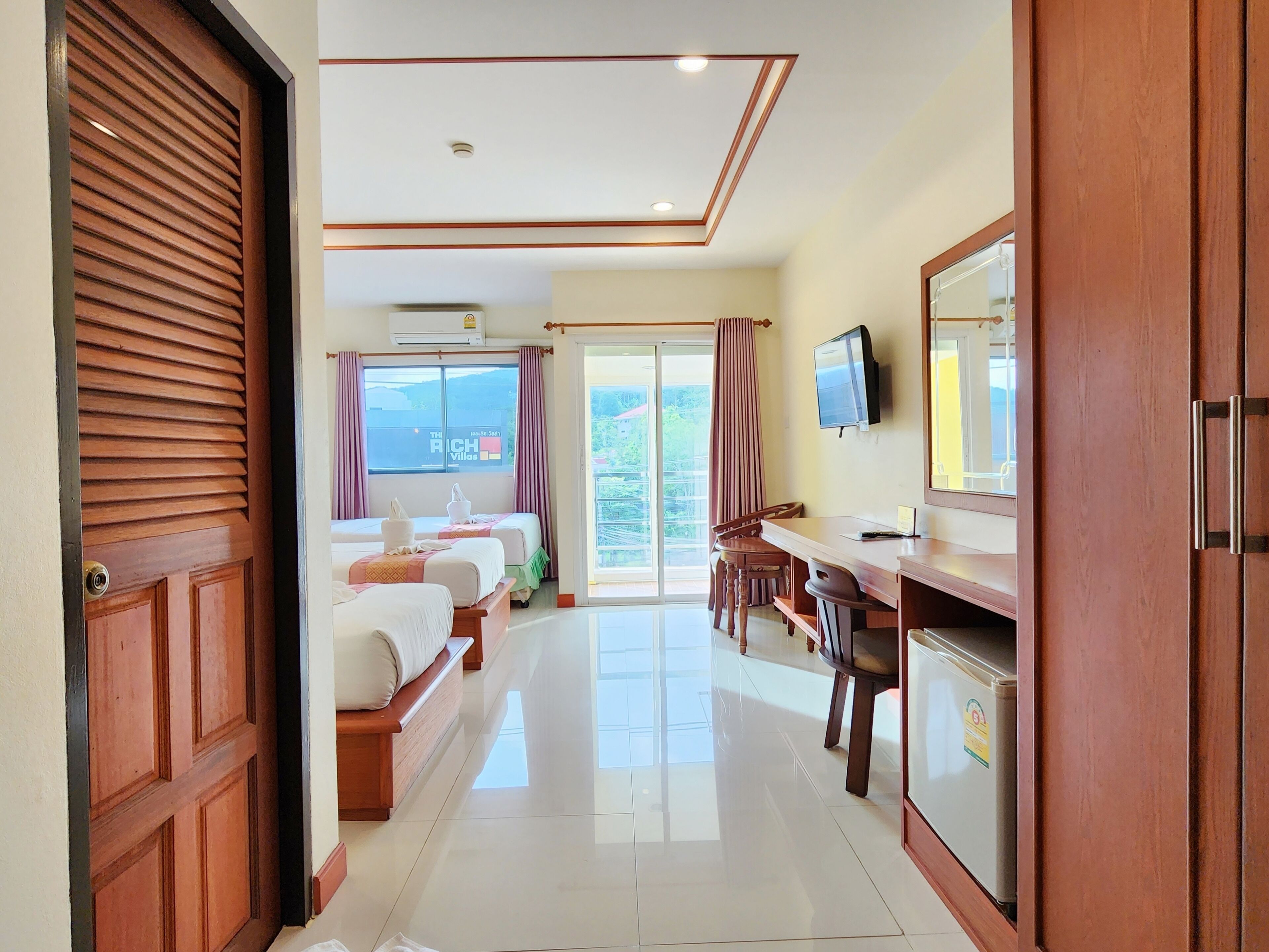 A hotel room with two beds, a desk, a TV, and a sliding glass door to the balcony.
