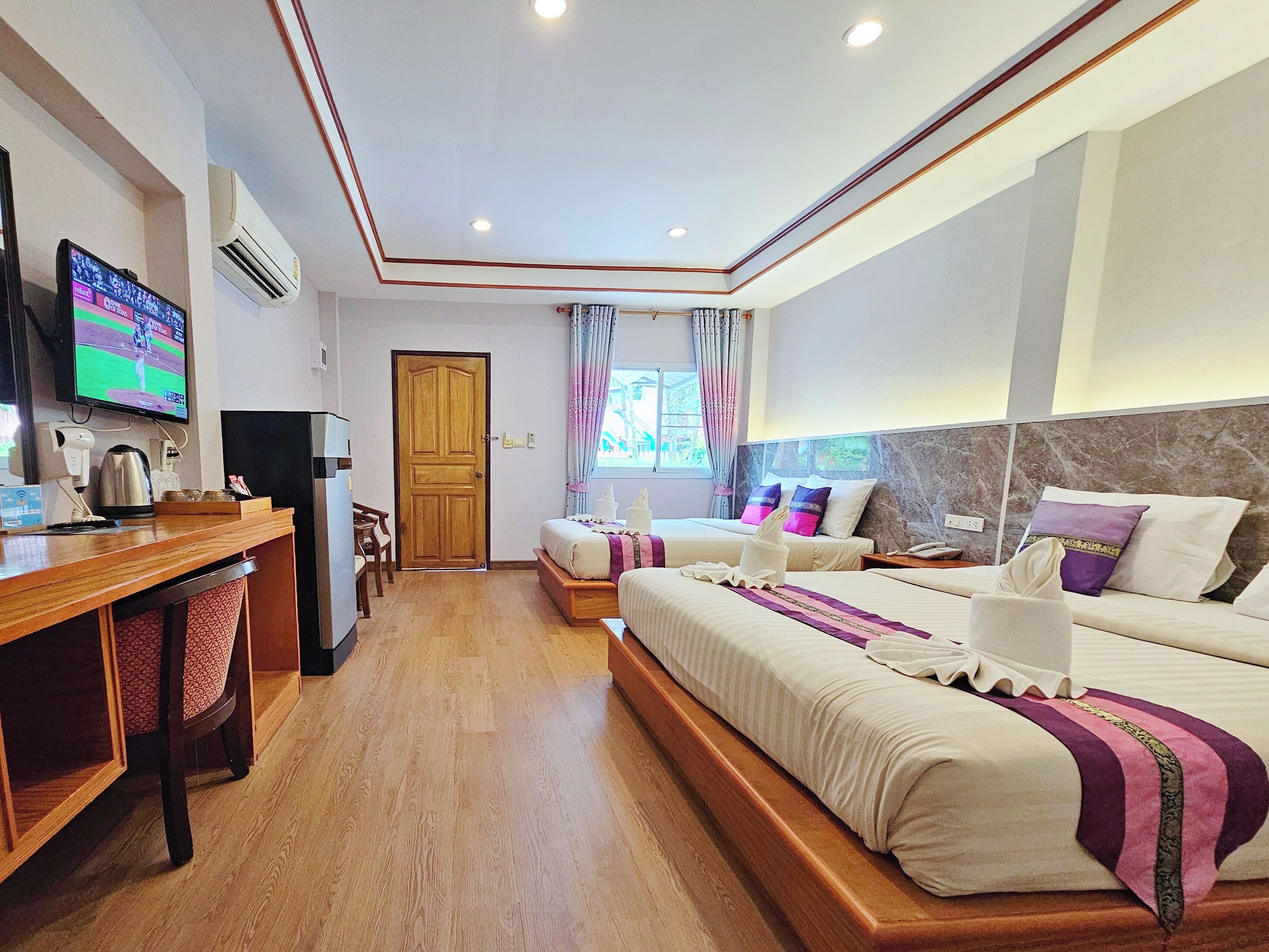 Een hotelkamer met twee bedden, een bureau met een computer, een televisie en een airconditioning.
