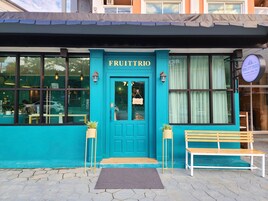 A storefront with a teal facade, a sign reading "FRUITTRIO," and a bench outside.