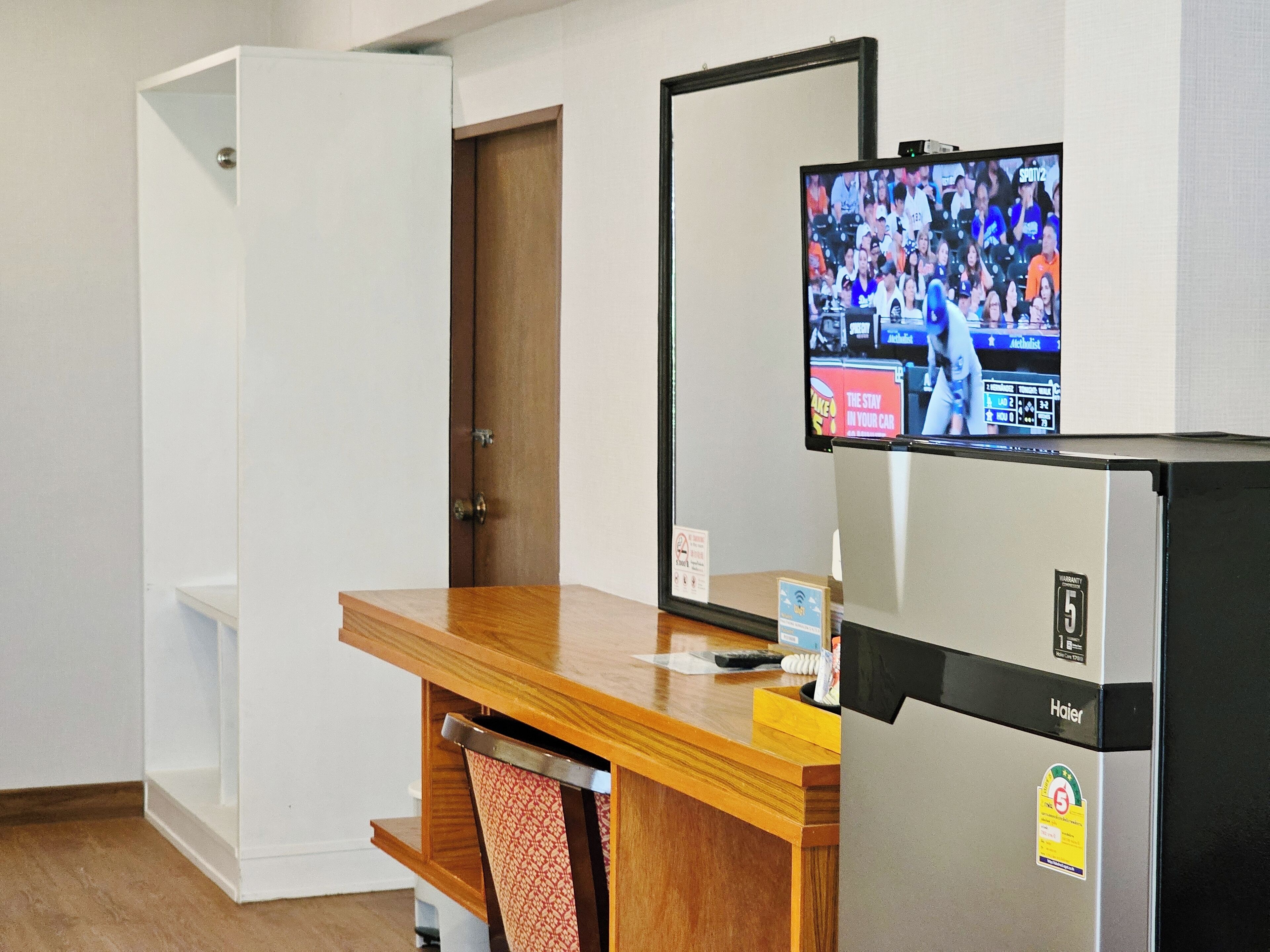 A hotel room with a wooden desk, a refrigerator, and a television displaying a sports event.