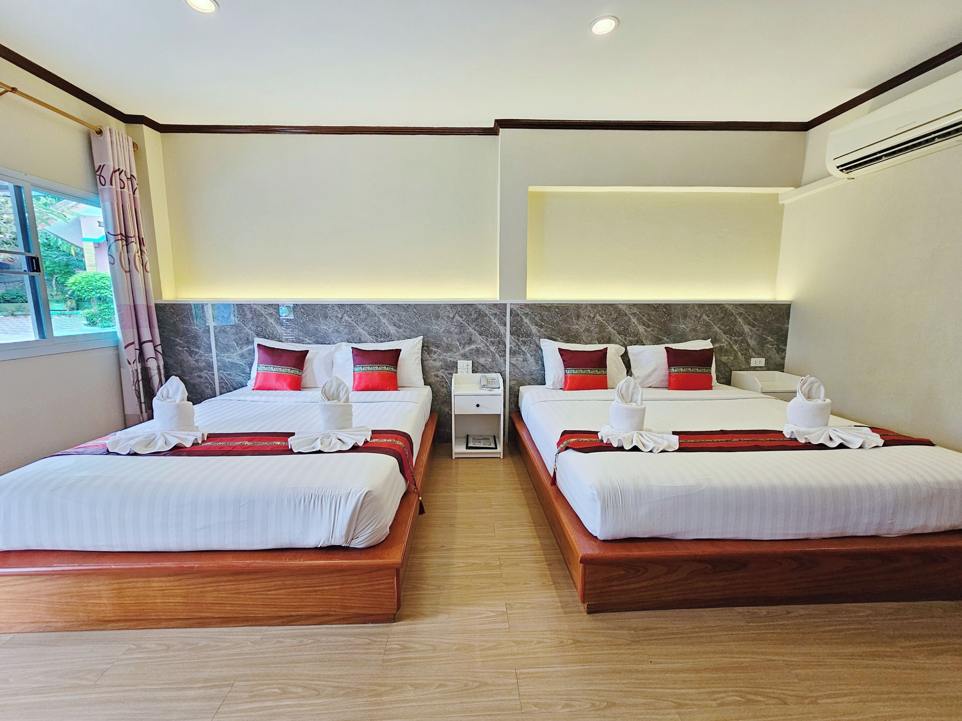 A hotel room with two beds, marble headboards, wooden flooring, and a window with curtains.