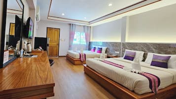 Habitación de hotel con un escritorio de madera, dos camas con almohadas moradas, un espejo grande y un televisor.