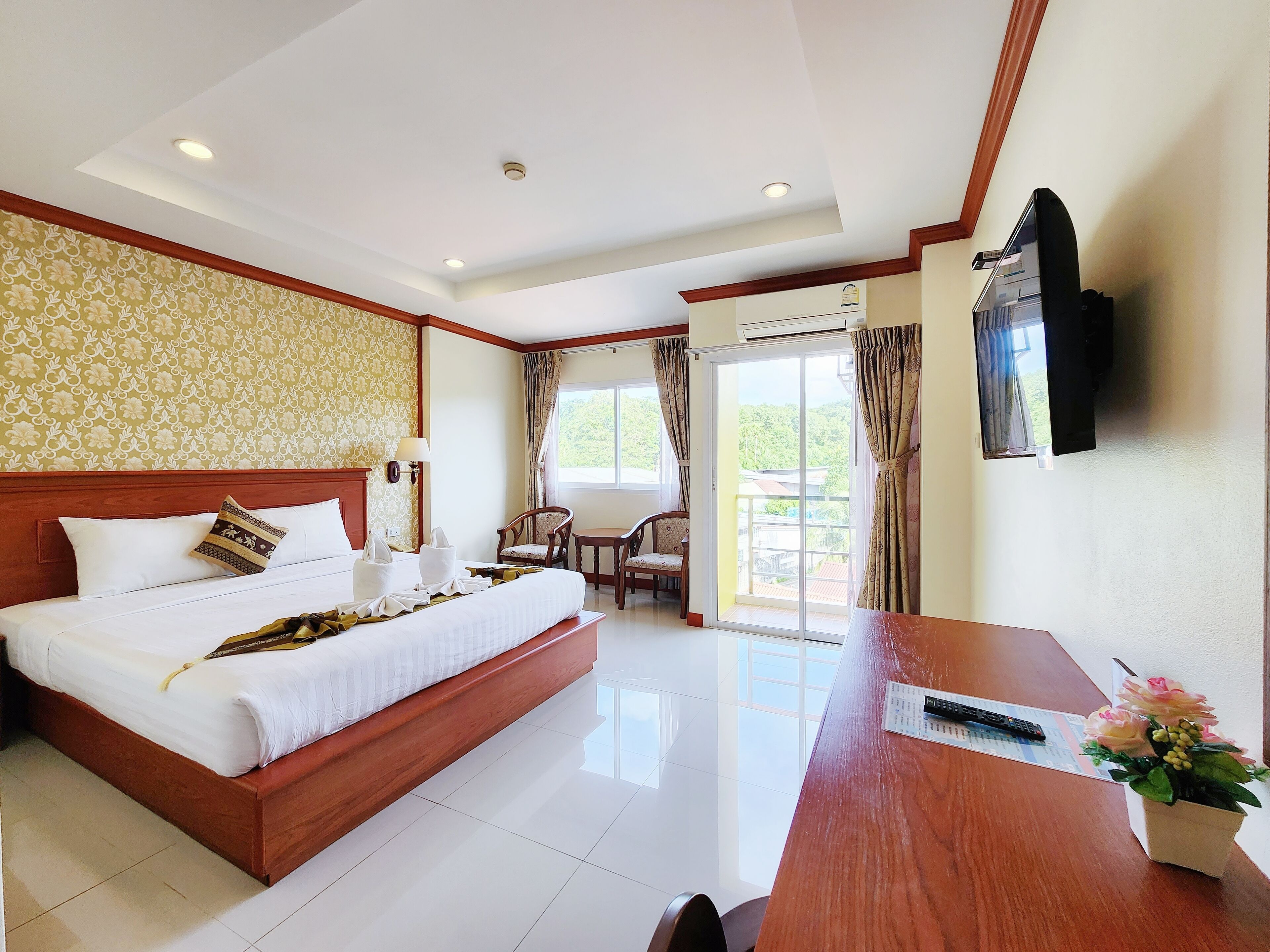 A hotel room with a large bed, a desk, a chair, a TV, and a balcony with a view.